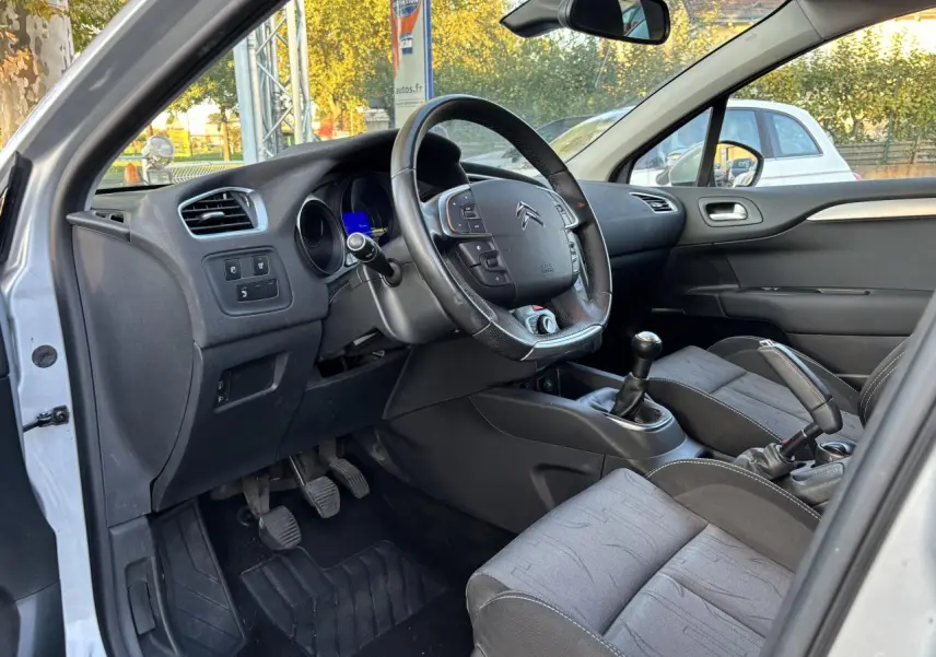 Intérieur côté conducteur d'une Citroën C4 gris clair 2012, volant multifonctions et boîte manuelle visibles.