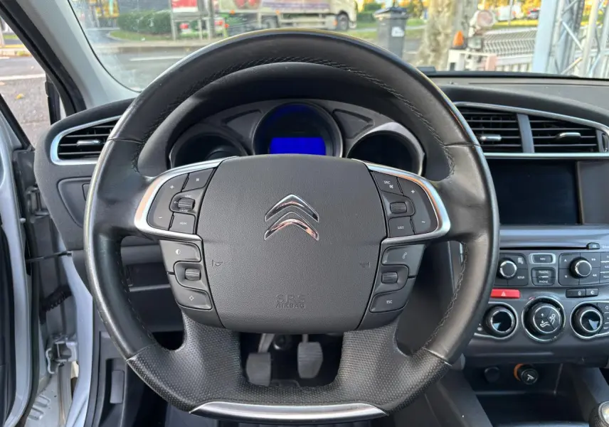 Vue intérieure centrée sur le volant multifonction noir de la Citroën C4 gris clair de 2012 avec tableau de bord visible.