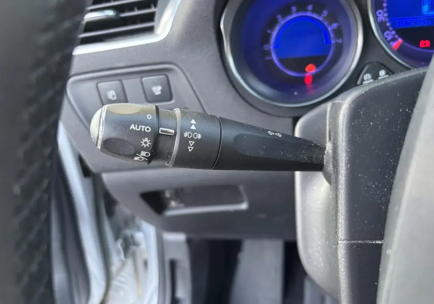 Gros plan sur la manette des phares et clignotants du tableau de bord d'une Citroën C4 gris clair de 2012.