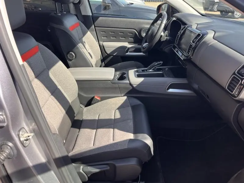 Vue intérieure côté conducteur du Citroën C5 Aircross gris, avec sièges tissu gris et bande rouge, tableau de bord moderne.