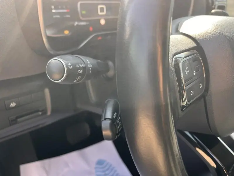Gros plan sur le volant cuir noir et la commande des phares à gauche dans l’habitacle du Citroën C5 Aircross gris.