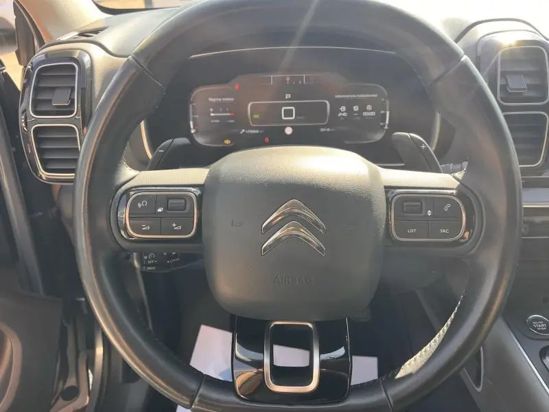 Vue rapprochée du volant cuir noir multifonction d’un Citroën C5 Aircross gris avec tableau de bord numérique en arrière-plan.