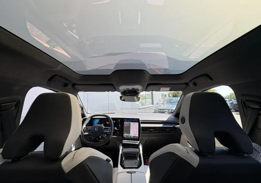 Vue intérieure avant du Renault Espace 2025, sièges gris sable clair et toit panoramique en verre opacifiant.