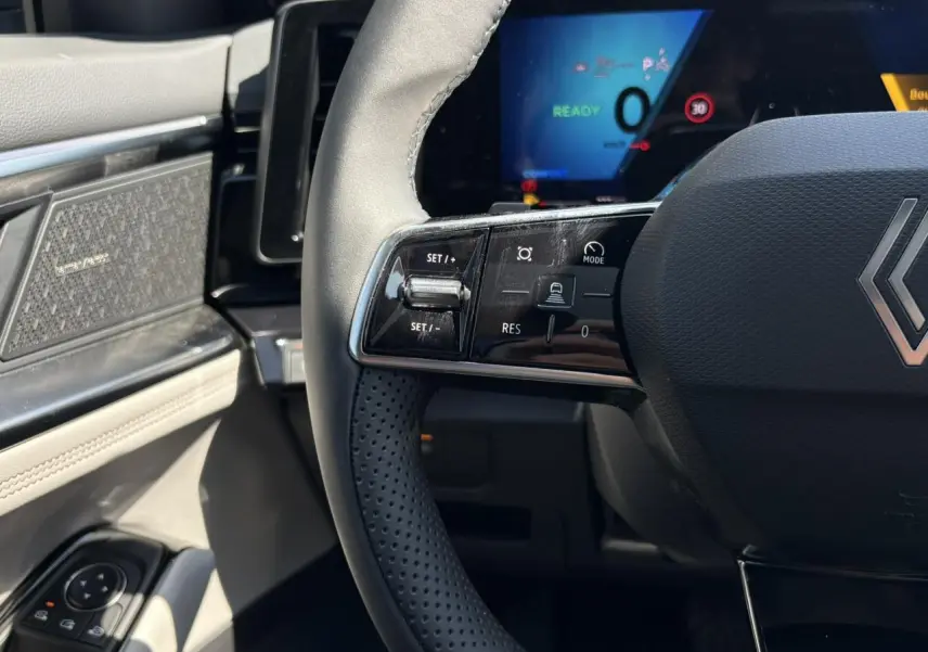 Gros plan sur le volant noir perforé et la planche de bord gris sable clair du Renault Espace VI hybride 2025.