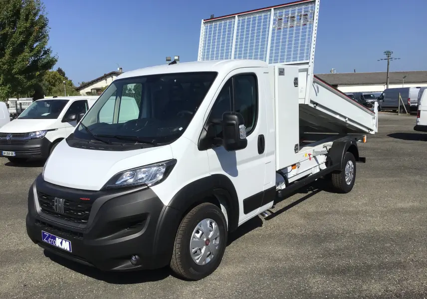 Fiat Ducato Chassis Benne blanc vu en 3/4 avant droit, benne acier relevée et coffre latéral visible.