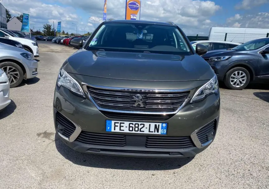 Vue avant d'un Peugeot 5008 gris clair garé en extérieur, avec calandre chromée et plaque d'immatriculation française visible.
