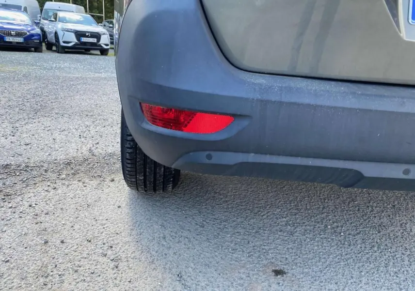 Gros plan sur le pare-chocs arrière gris clair du Peugeot 5008 avec feu rouge et capteurs de recul visibles.