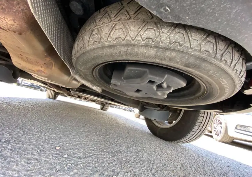 Vue en contre-plongée sous un Peugeot 5008 gris clair, mettant en valeur la roue de secours galette sous le véhicule.