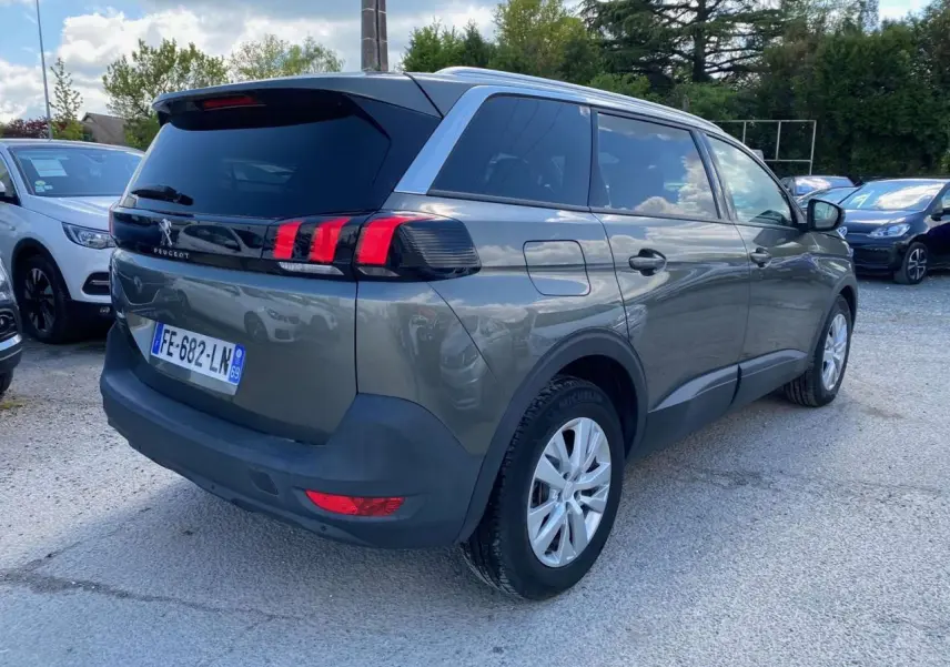 Peugeot 5008 gris clair vue 3/4 arrière droit, feux arrière à griffes rouges et vitres surteintées.