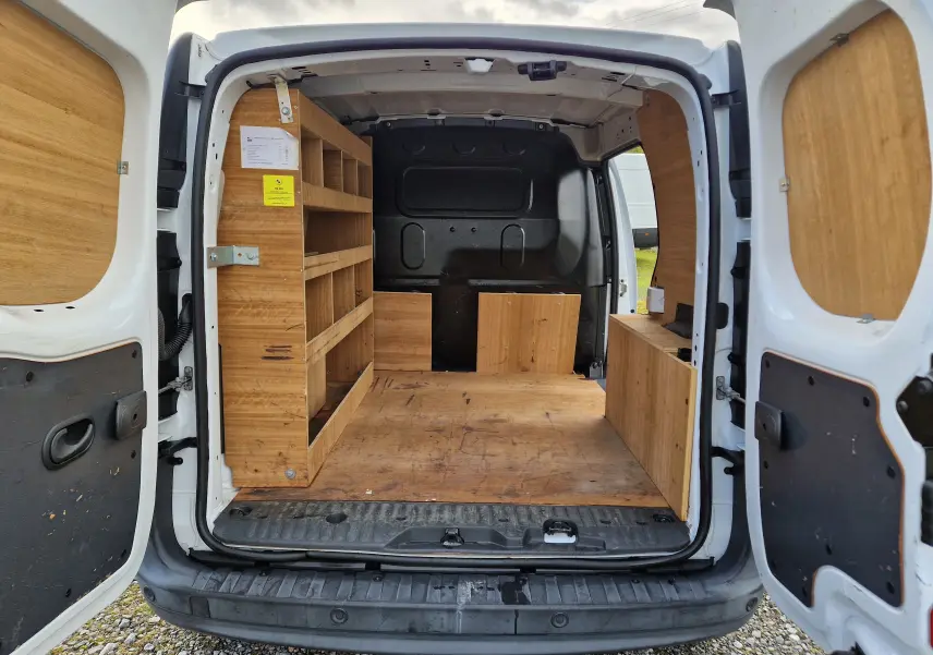 Vue arrière ouverte du Renault Kangoo blanc 2020, montrant l'aménagement intérieur en bois avec étagères et rangements.