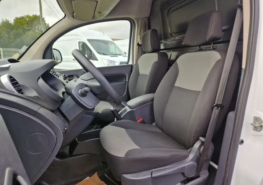 Vue intérieure côté conducteur du Renault Kangoo blanc 2020, montrant les sièges avant gris et la console centrale avec levier de vitesse manuel.