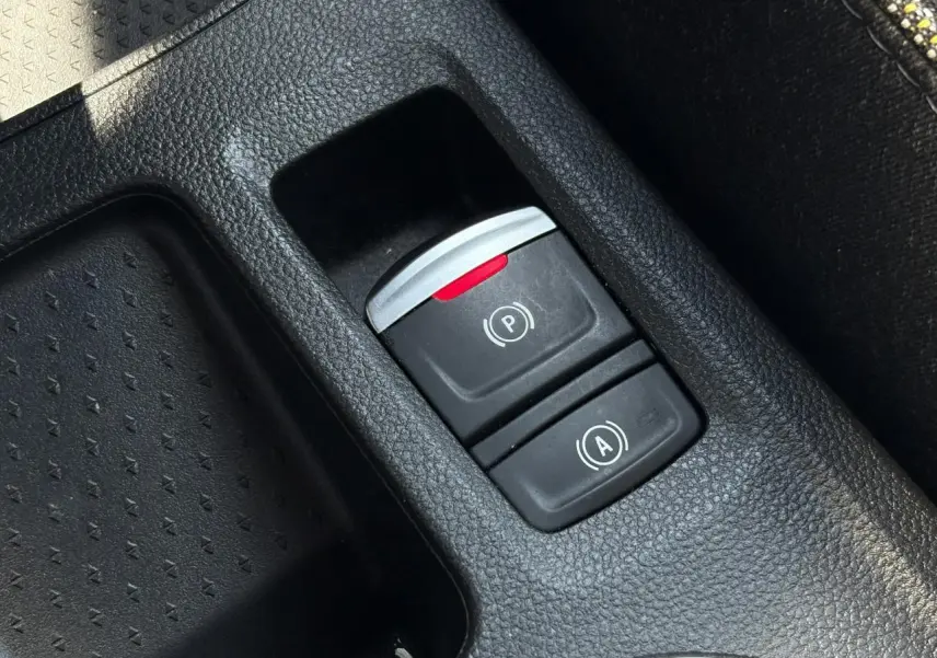 Gros plan sur les commandes du frein de parking électrique et de l’auto-hold dans la console centrale d’une Renault Symbioz noire.