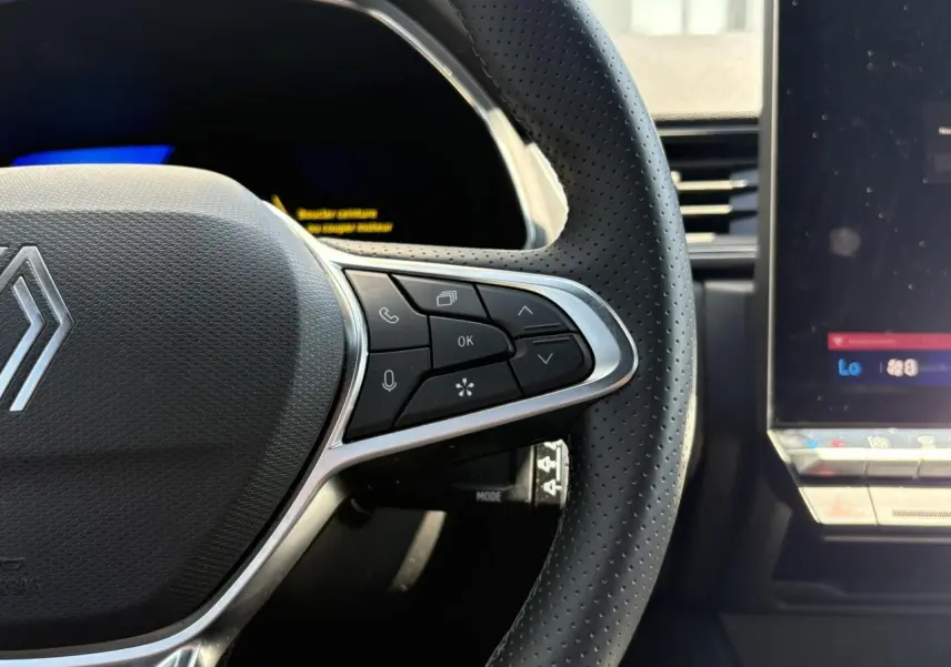 Gros plan sur le côté droit du volant perforé noir du Renault Symbioz 2025 avec commandes intégrées et écran tactile adjacent.