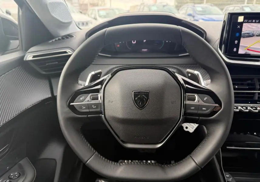 Vue rapprochée du volant noir de la Peugeot 208 Hybrid 145 Allure 2025 avec commandes intégrées et tableau de bord numérique.