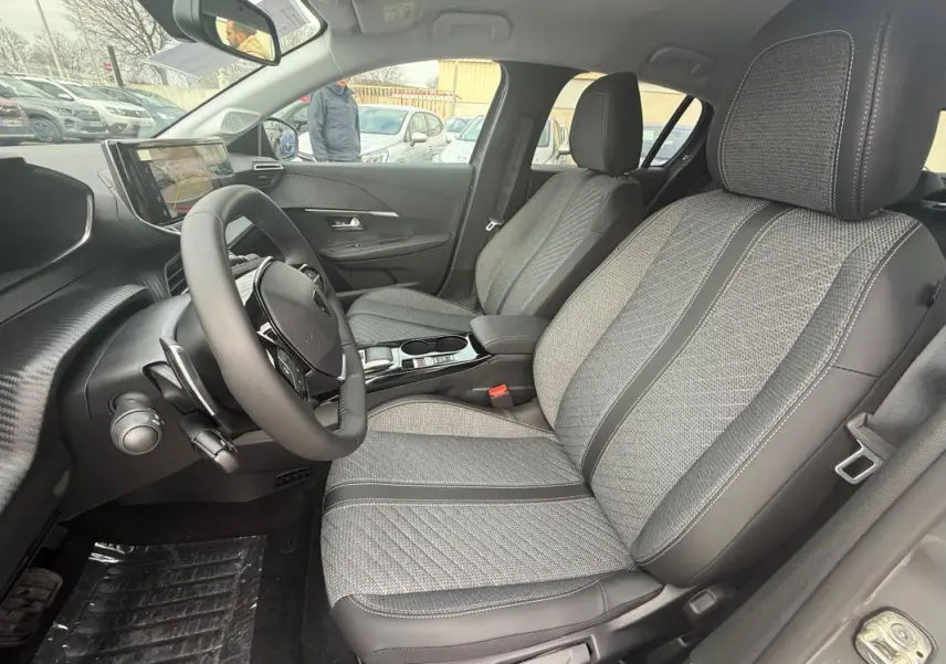 Vue intérieure côté conducteur de la Peugeot 208 Hybrid 145 gris, mettant en valeur les sièges tissu et le volant multifonction.