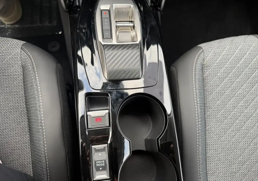 Vue plongeante sur la console centrale noire brillante de la Peugeot 208 Hybrid 145, avec levier de vitesses et porte-gobelets.