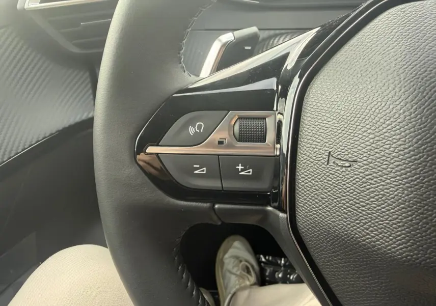 Gros plan sur les commandes gauche du volant noir du Peugeot 208 Hybrid 145 gris, avec bouton volume et Bluetooth.