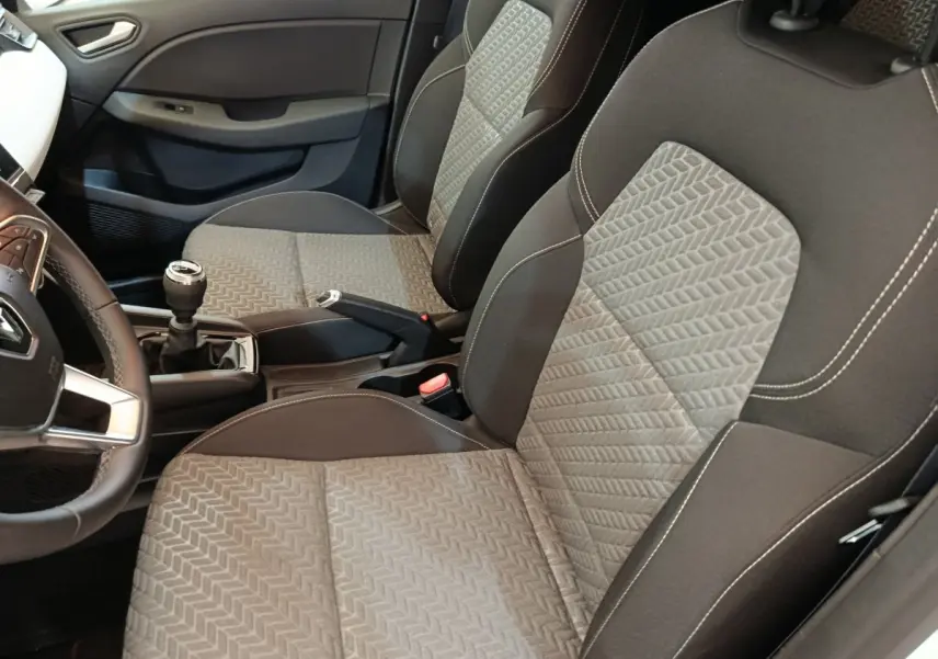 Vue intérieure côté conducteur de la Renault Clio Evolution TCe 90 2023, sièges tissu gris et volant cuir synthétique.