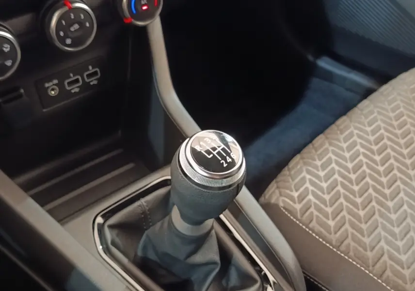 Gros plan sur le levier de vitesses manuel noir et argenté de la Renault Clio Evolution TCe 90, avec siège tissu gris à motifs.