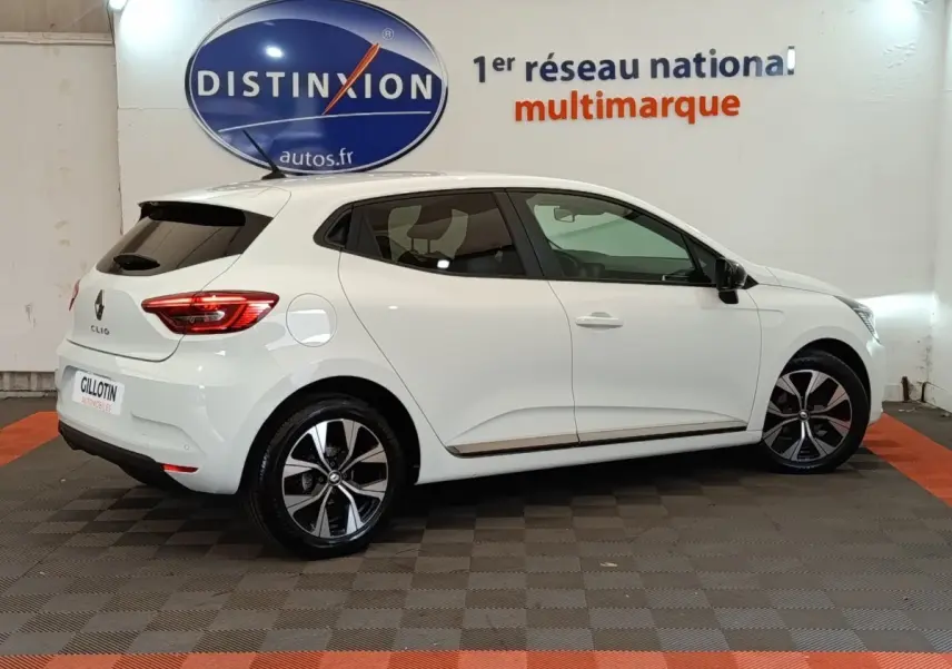 Profil droit d'une Renault Clio Evolution TCe 90 blanche 2023 avec jantes alliage et vitres teintées, en intérieur showroom.