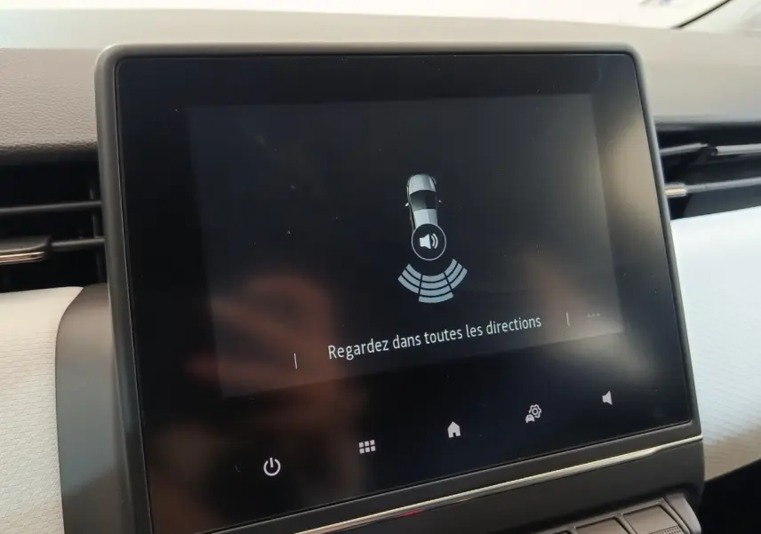 Écran tactile central de la Renault Clio blanc 2023 affichant l'alerte de surveillance des angles morts.
