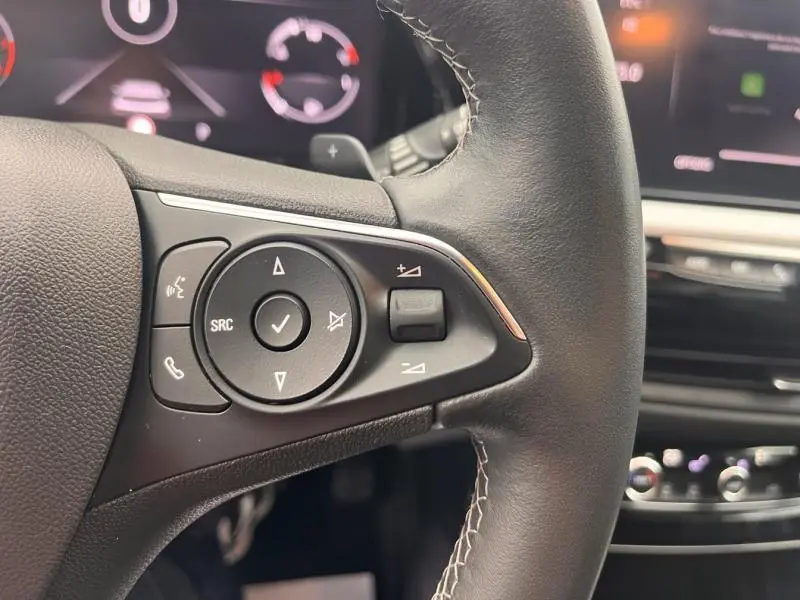 Gros plan sur les commandes au volant cuir noir du côté gauche de l’Opel Grandland 2023, avec tableau de bord flou en arrière-plan.