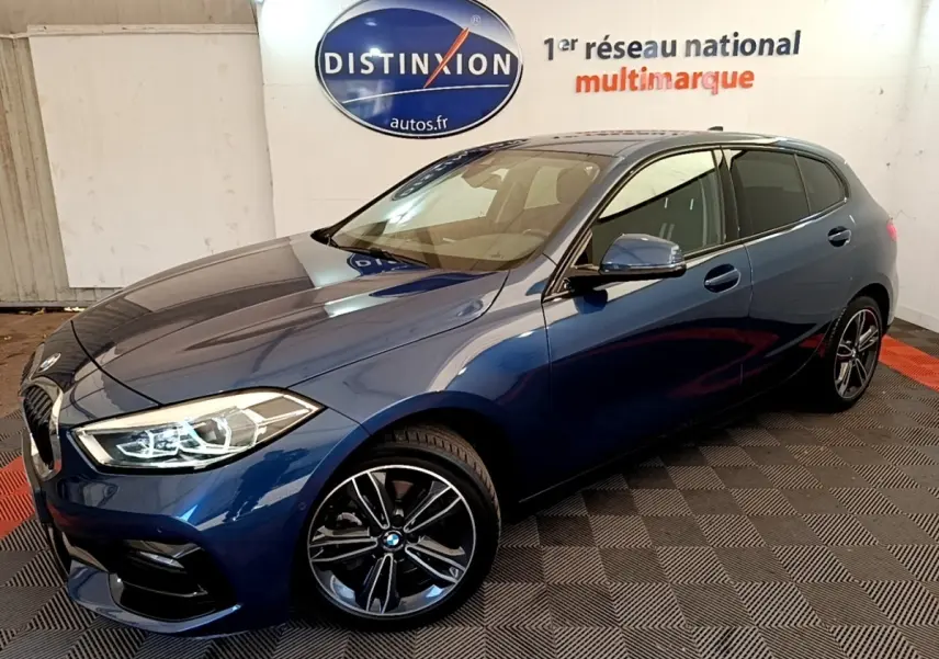 BMW Série 1 118i Edition Sport bleu vue 3/4 avant droit, avec phares LED et jantes alliage noires.