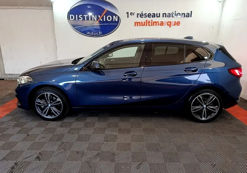 Profil côté gauche d’une BMW Série 1 118i Edition Sport bleu, avec jantes alliage et vitres teintées.