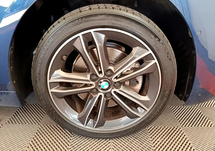 Gros plan sur la roue avant droite avec jante alliage BMW et carrosserie bleu de la Série 1 118i Edition Sport.