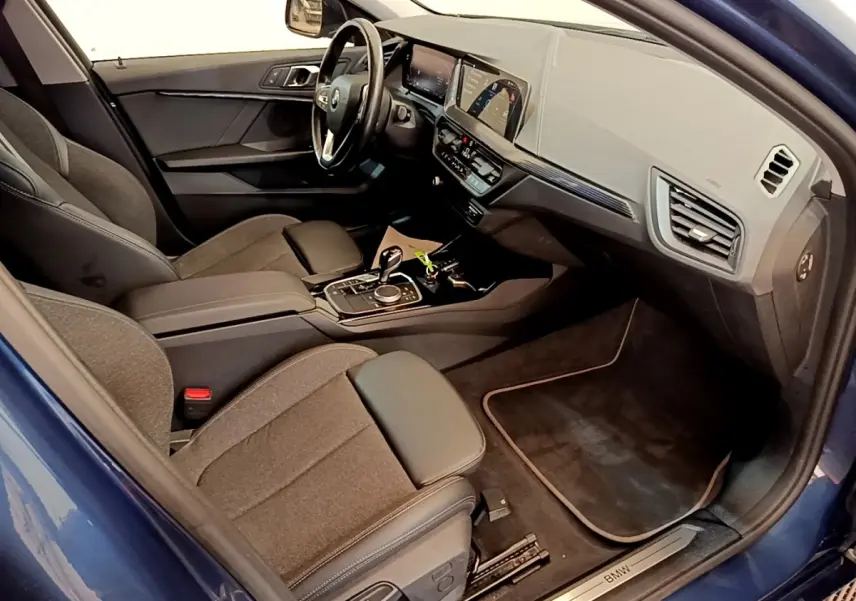 Intérieur BMW Série 1 118i bleu, vue côté passager avant, tableau de bord moderne avec écran tactile couleur.