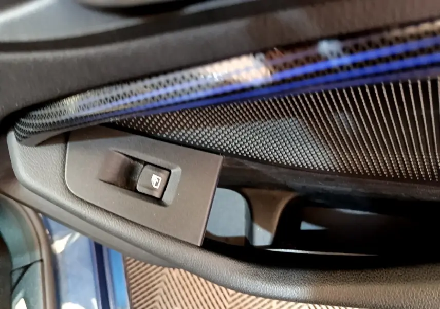 Gros plan sur le bouton de commande de la vitre électrique côté conducteur, intérieur bleu et noir de la BMW Série 1 118i Edition Sport.