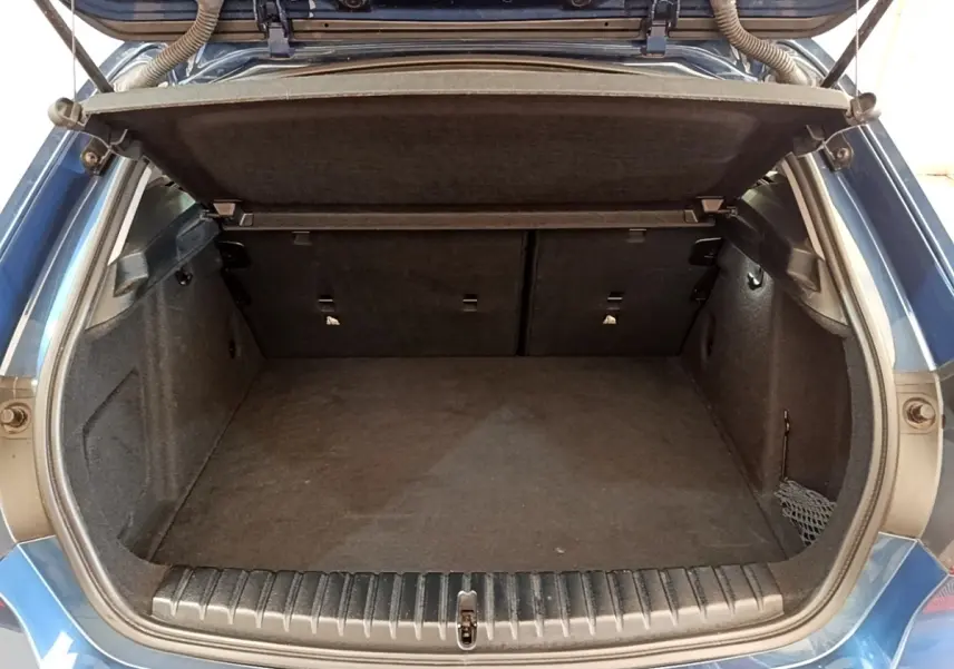 Coffre ouvert vu de l'arrière d'une BMW Série 1 118i bleu, montrant l'espace de chargement vide et la tablette cache-bagages.
