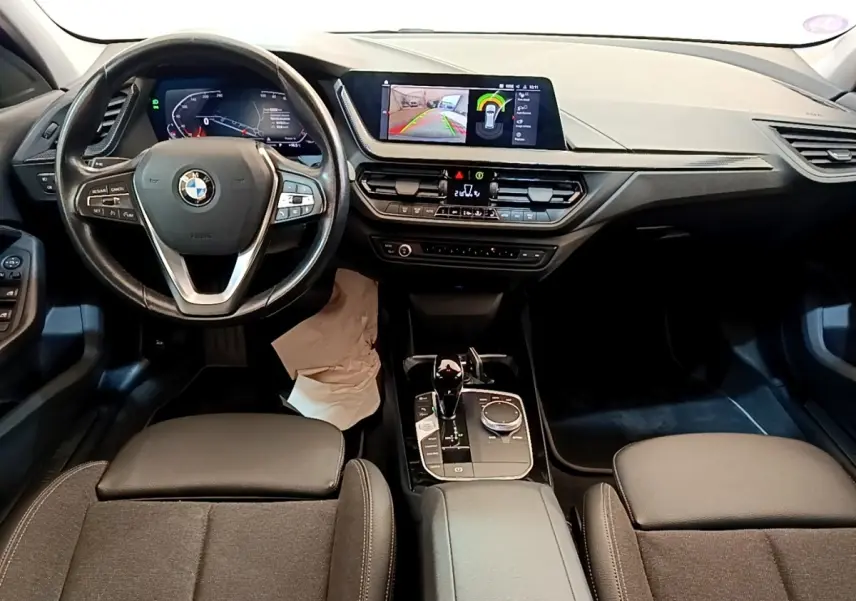 Vue intérieure avant de la BMW Série 1 118i Edition Sport 2023, tableau de bord avec écran tactile et volant multifonction.