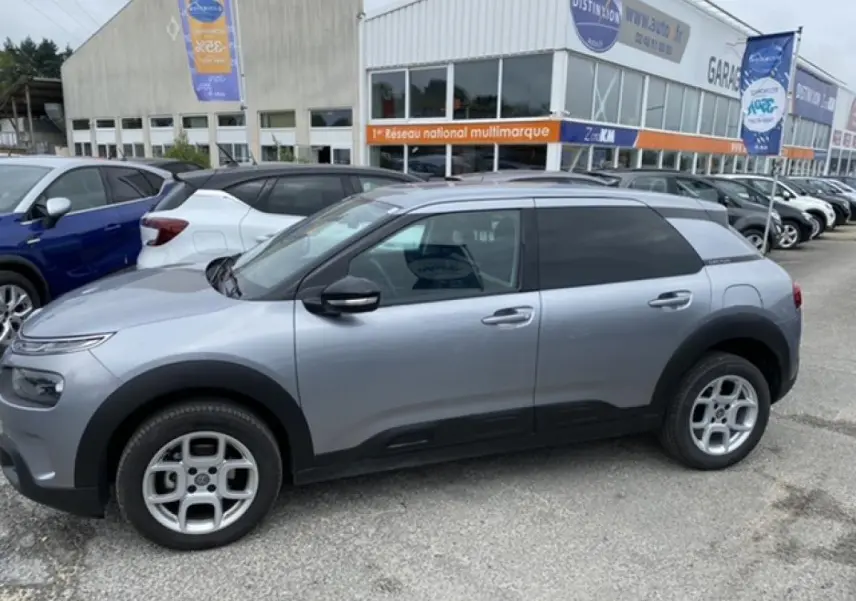 Profil côté gauche d'une Citroën C4 Cactus gris clair 2020 avec protections noires et jantes alliage au parking.