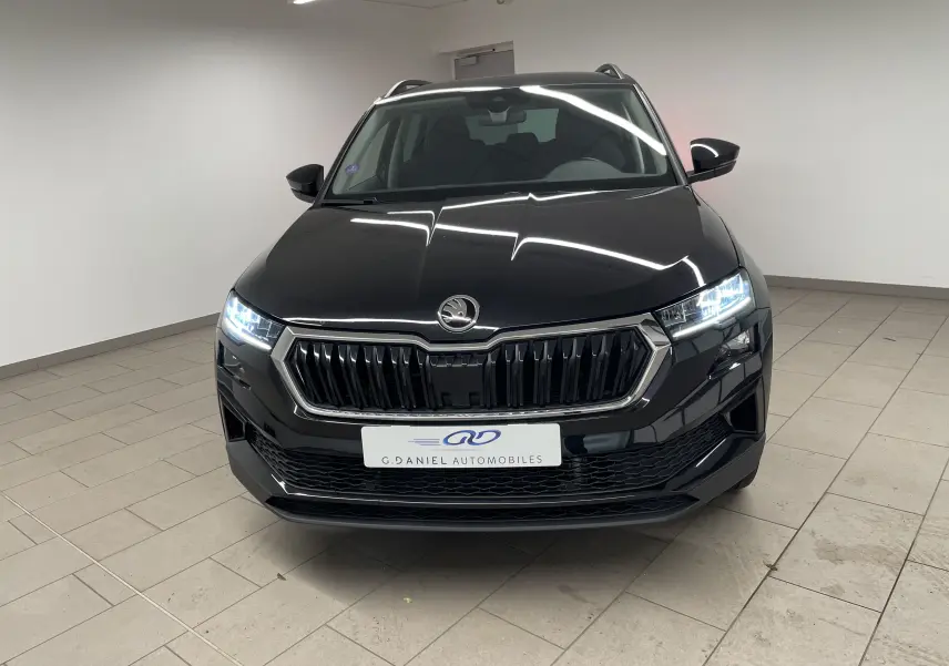 Vue frontale d'un Skoda Karoq noir Magic Nacre 2023 avec phares LED allumés dans un showroom.