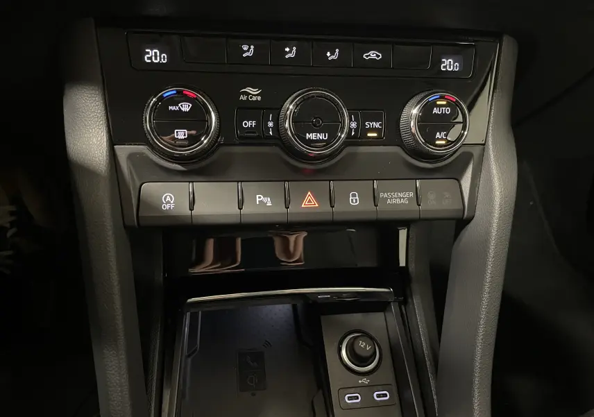 Gros plan sur la console centrale du Skoda Karoq noir Magic nacré, montrant les commandes climatisation et la zone Phonebox avec recharge sans fil.