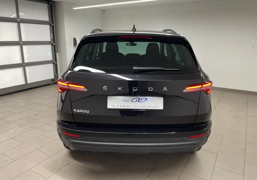 Vue arrière d'un Skoda Karoq noir Magic nacré avec feux allumés dans un garage intérieur.