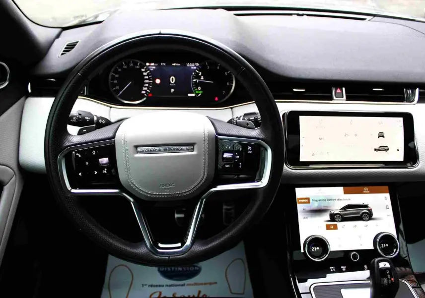 Intérieur du Range Rover Evoque 2023, vue de face sur le tableau de bord clair avec écran tactile et volant noir.