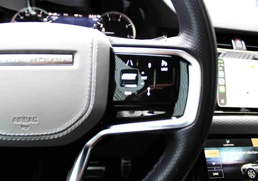 Vue rapprochée du volant cuir noir et beige du Range Rover Evoque 2023 avec commandes intégrées et tableau de bord digital.
