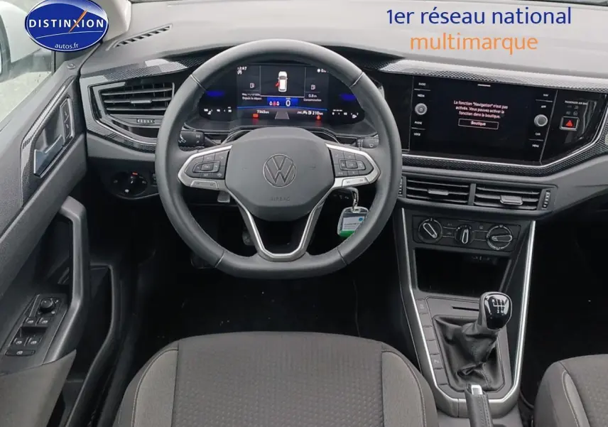 Vue intérieure centrée sur le volant multifonction et la console avec levier de vitesses manuelle d'une Volkswagen Polo blanche.