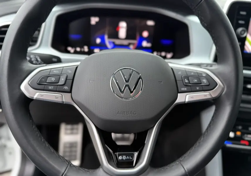 Gros plan sur le volant multifonction noir du Volkswagen T-Roc 2.0 TDI 150CH LIFE PLUS 2025 avec tableau de bord numérique flou en arrière-plan.