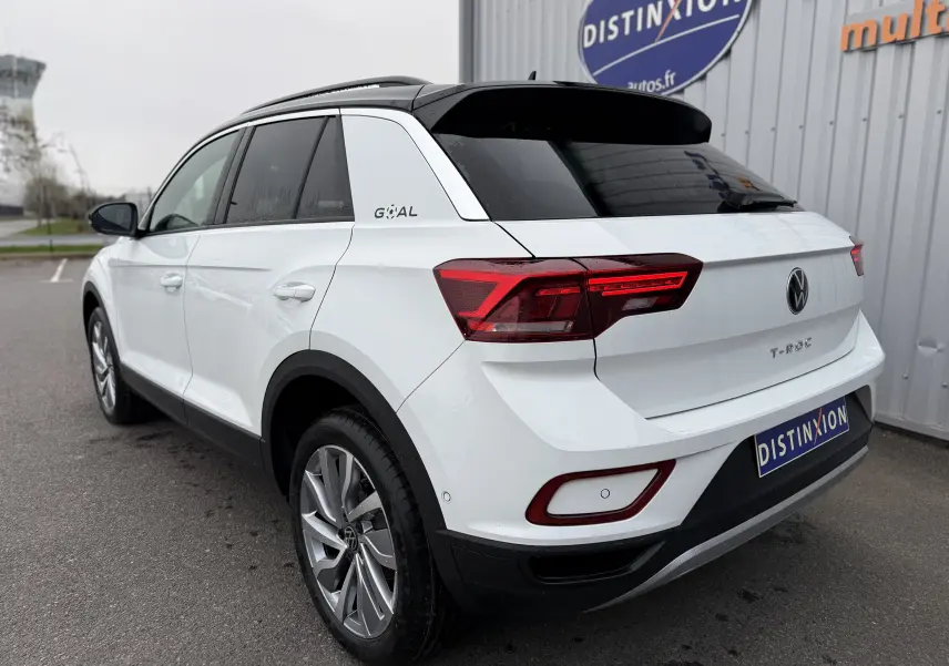 Vue 3/4 arrière droite d’un Volkswagen T-Roc blanc Pure avec toit noir, feux arrière LED et jantes alliage.