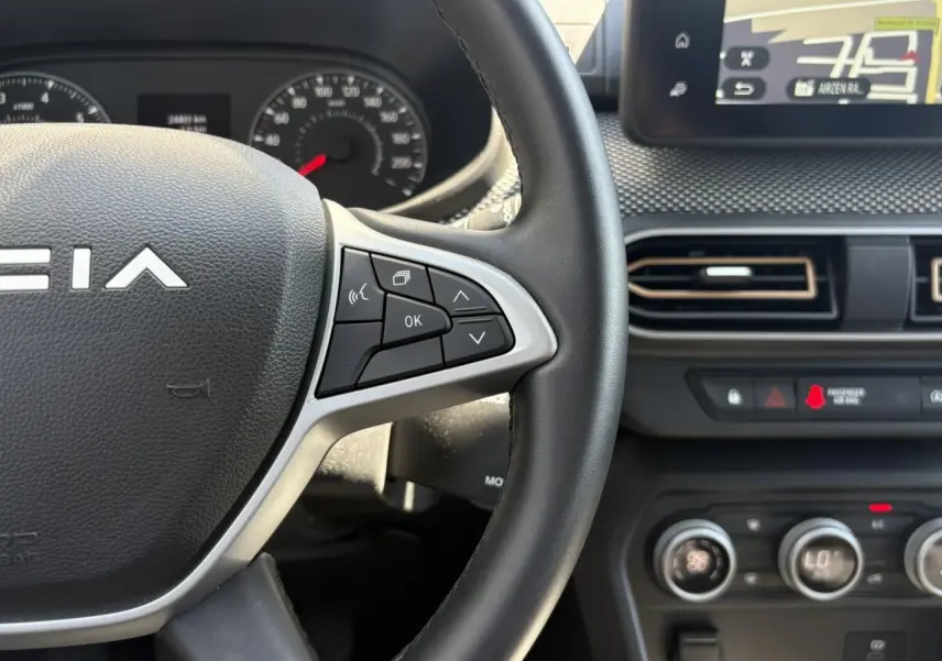 Gros plan sur le volant noir de la Dacia Sandero Stepway 2025 avec commandes multifonctions et écran tactile GPS visible.