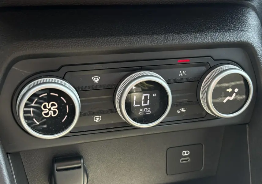 Gros plan sur les commandes de climatisation automatique du Dacia Sandero Stepway beige, avec affichage digital et réglages rotatifs.