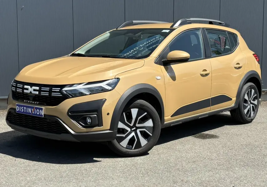 Vue 3/4 avant droite d'une Dacia Sandero Stepway beige Safari avec barres de toit et jantes spécifiques.
