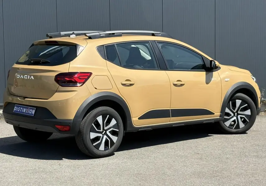 Dacia Sandero Stepway beige Safari vue 3/4 arrière droit avec barres de toit et jantes noires et argentées.