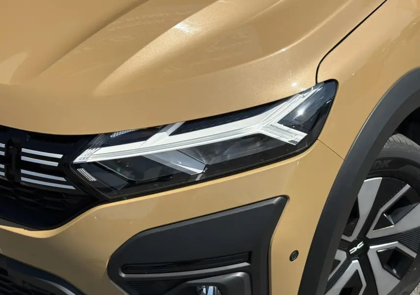 Gros plan sur l'avant droit beige Safari du Dacia Sandero Stepway 2025, mettant en valeur le phare LED et la roue avec enjoliveur.