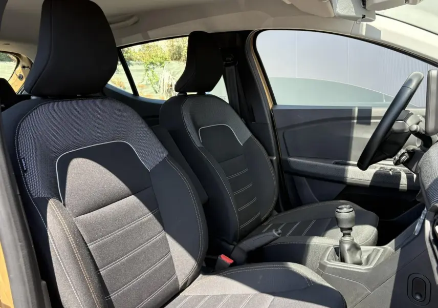 Vue intérieure côté conducteur de la Dacia Sandero Stepway beige Safari, montrant les sièges et levier de vitesses manuel.