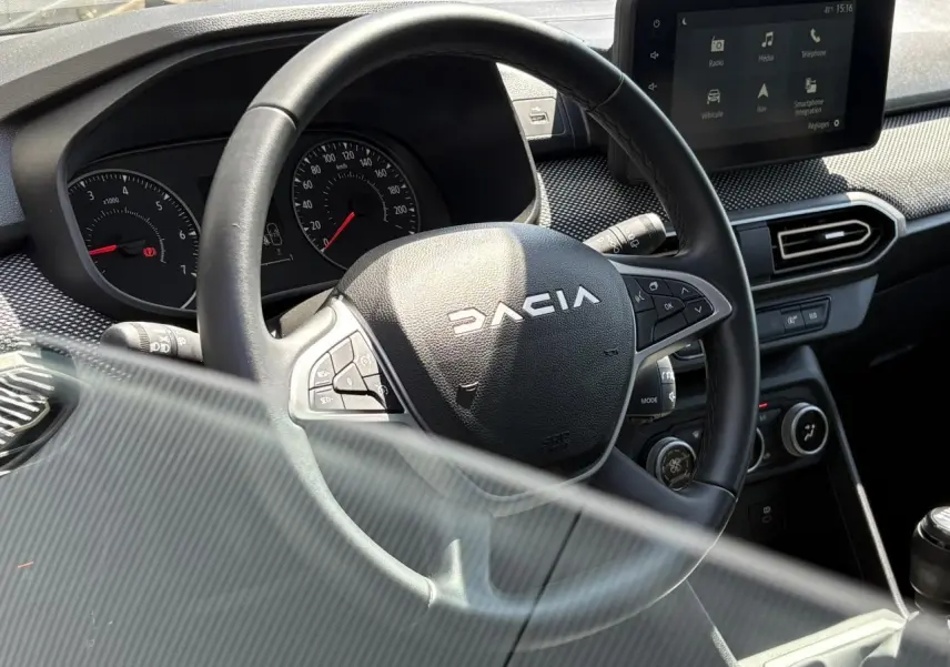 Vue rapprochée du volant noir Dacia et du tableau de bord avec écran tactile dans l'habitacle du Sandero Stepway 2025.
