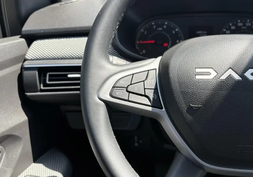 Gros plan sur le volant noir de la Dacia Sandero Stepway 2025 avec commandes intégrées côté gauche et tableau de bord partiel.